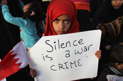 Criança com cartaz “Silence is a war crime” (“O silêncio é um crime de guerra”) - Retirada de facebook grupo “operation bahrain”