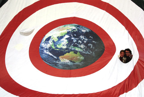 Manifestantes ambientalistas aparecem no buraco de uma bandeira gigante durante manifestação ambientalista em Bali. Foto Lusa/EPA/MAST IRHAM