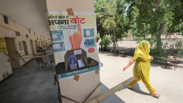 Mulher passa em frente de um cartaz eleitoral na Índia. 