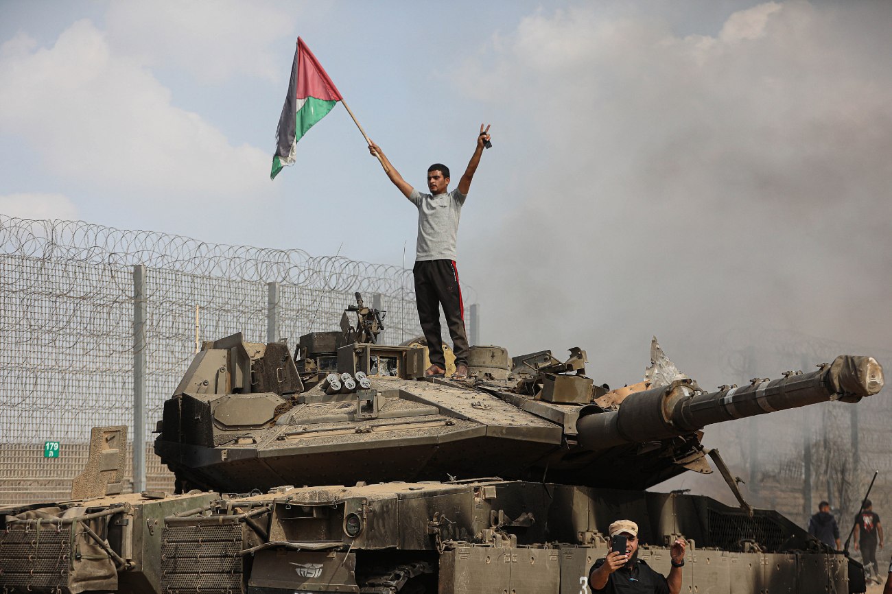 Palestinianos em cima e ao lado de um tanque israelita dentro da cerca da fronteira com Israel na cidade de Khan Younis, sul da Faixa de Gaza, 7 de outubro de 2023. (Yousef Mohammed/Flash90)