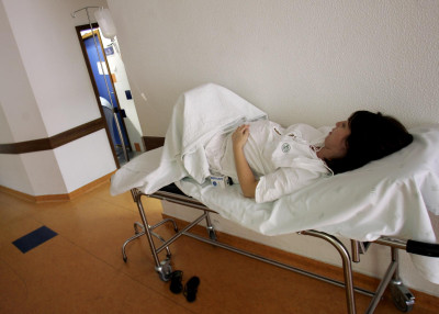 Grávida deitada numa maca no corredor de um hospital.