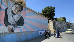 Vendedor ambulante expõe bandeiras e posters dos líderes talibãs junto a um mural de uma menina na escola.