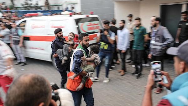 Profissional de saúde carrega criança palestiniana para dentro de hospital.