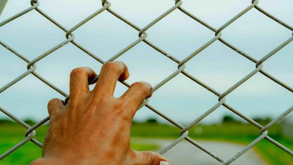 Mão a segurar rede de arame de metal. Conceito de refugiado e migrante