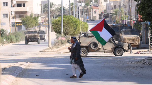 Homem passa com bandeira palestiniana por veículos militares em Tulkarem, Cisjordânia.