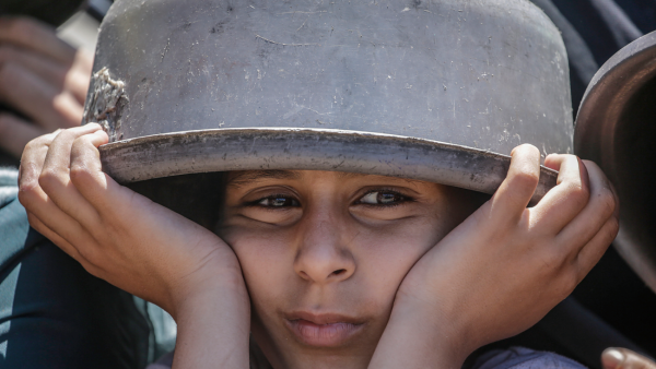 Uma menina palestina deslocada internamente, com um tacho vazio sobre a cabeça, espera para receber comida de uma cozinha de caridade, na cidade de Gaza.