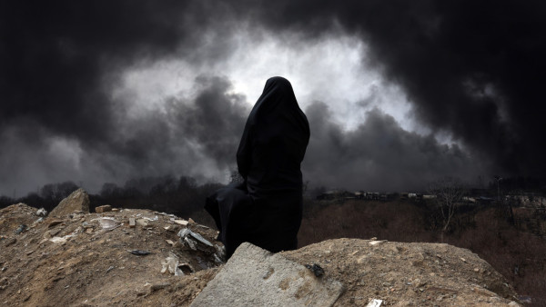 Uma mulher iraniana com véu, membro do Crescente Vermelho do Irão, observa o fumo que ainda se eleva da refinaria de petróleo de Shahran após um ataque aéreo 