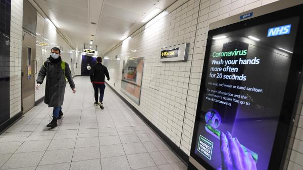 Anúncio do Serviço Nacional de Saúde britânico numa estação de metro de Londres,  março de 2020. Foto de ANDY RAIN/EPA/LUSA.