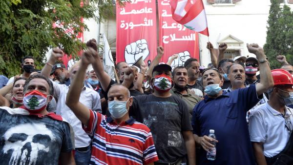 Manifestantes libaneses em frente a duas faixas de que dizem "Beirute Capital da Revolução" e "Beirute Capital sem armas". Agosto de 2020. Foto de WAEL HAMZEH/EPA/Lusa.