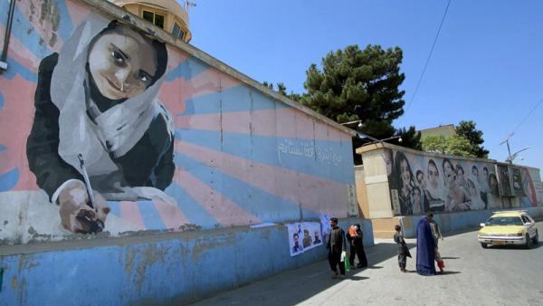 Vendedor ambulante expõe bandeiras e posters dos líderes talibãs junto a um mural de uma menina na escola.