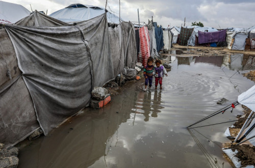 Crianças palestinas caminham perto das suas tendas inundadas após uma tempestade, em Khan Younis, em 28 de dezembro de 2025. 