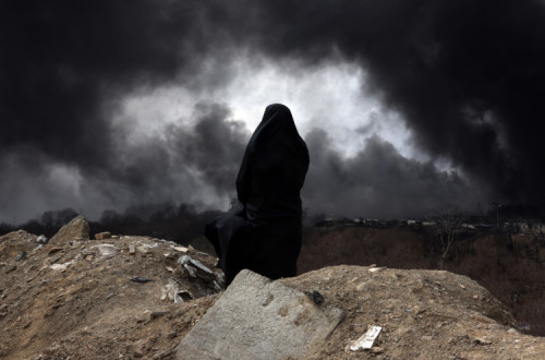 Uma mulher iraniana com véu, membro do Crescente Vermelho do Irão, observa o fumo que ainda se eleva da refinaria de petróleo de Shahran após um ataque aéreo 