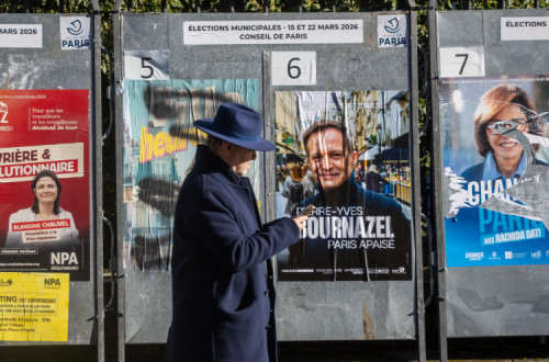 Eleitor passa unto a cartazes eleitorais no dia da primeira volta das municipais francesas.