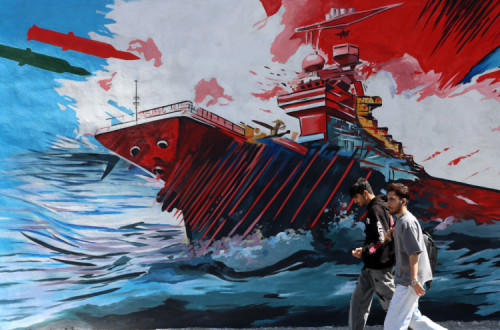 Jovens passam por um mural anti-EUA e Israel em Teerão.