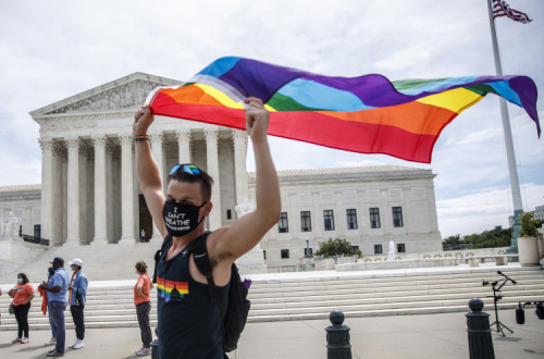 Homem celebra a decisão do Supremo Tribunal dos EUA com bandeira arco-íris à porta desta instituição. Foto de SHAWN THEW/EPA/Lusa.