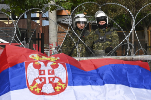 Soldados da Nato em frente a uma bandeira sérvia. Foto de GEORGI LICOVSKI/EPA/Lusa.