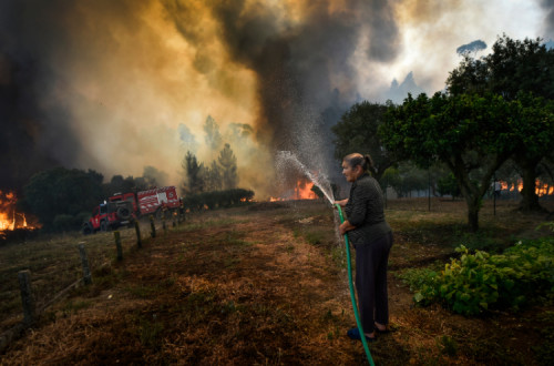 Uma mulher molha o terreno na aldeira do Lavradio durante um incêndio florestal, no concelho de Ourém. Este incêndio começou há uma semana, a 7 de julho de 2022. Foto de Nuno André Ferreira/ Lusa, de 13 de julho de 2022