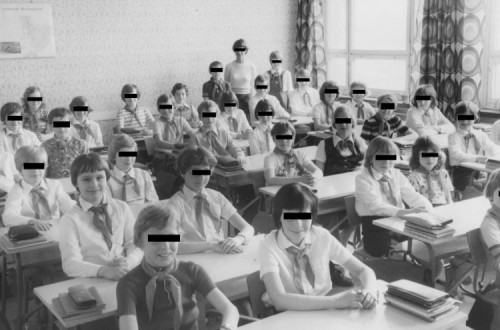 Crianças numa sala de aula com uma barra preta sobre os olhos, exceto uma, fotografia a preto e branco.